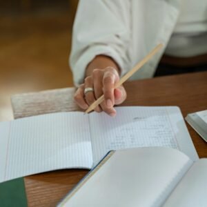 Close-up of a person writing in a graph notebook with a pencil at a wooden table, ideal for study and education themes.
